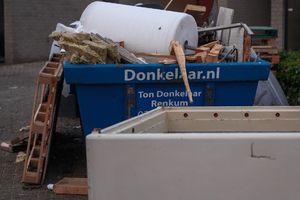 A dumpster accompanied by a white trash can and a blue trash can, positioned at a renovation site in Washington, DC.